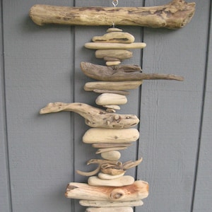 May include: A driftwood mobile with a long, horizontal piece of driftwood at the top and a series of smaller pieces of driftwood stacked vertically below it. The mobile is hanging from a ceiling or wall and is made of natural materials.
