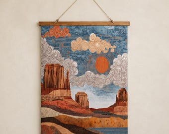 May include: A rectangular wall hanging featuring a woven desert landscape with tall red rock formations, a blue sky, and a bright orange sun. The scene includes stylized white and orange swirling clouds and is suspended by a wooden frame and rope.