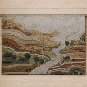 Puede incluir: Un tapiz rectangular con un diseño de paisaje texturizado en tonos beige, marrón, verde oliva y crema. La obra representa colinas superpuestas, senderos sinuosos y pequeños árboles circulares, suspendida de una varilla de madera superior.