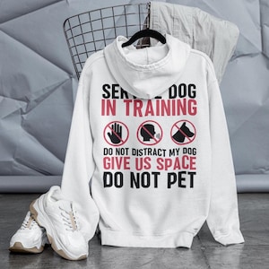 May include: White hoodie with a black graphic that says "Service Dog in Training" with three red circle icons that say "Do Not Distract My Dog, Give Us Space, Do Not Pet."