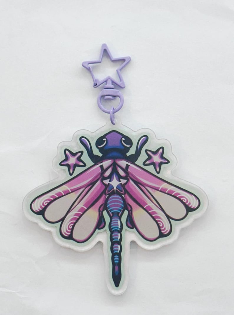 A purple, blue, and yellow colored acrylic dragonfly keychain with a plastic purple star chain surrounded by purple stars.