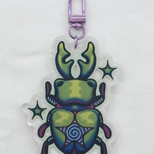 A green, blue, and purple colored acrylic stag beetle keychain with a purple metallic chain surrounded by green stars.