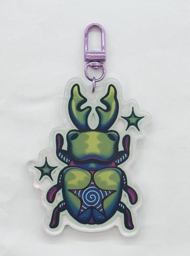 A green, blue, and purple colored acrylic stag beetle keychain with a purple metallic chain surrounded by green stars.
