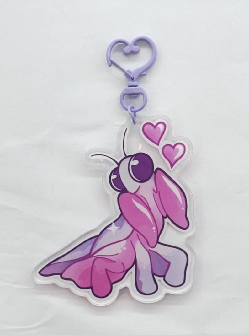 A purple and pink colored acrylic orchid mantis keychain with a plastic purple heart chain surrounded by pink hearts.