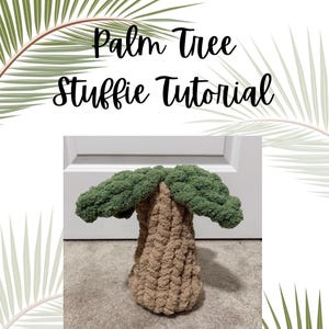 May include: A handmade, stuffed palm tree with a tan trunk and green leaves. The text "Palm Tree Stuffie Tutorial" is written above the tree. The tree is sitting on a gray surface, with palm fronds in the background.