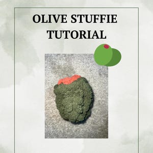 May include: An olive-shaped craft project with a red center, set against a textured background. The image includes the text "OLIVE STUFFIE TUTORIAL" in a bold, dark font, and a graphic of two green olives.