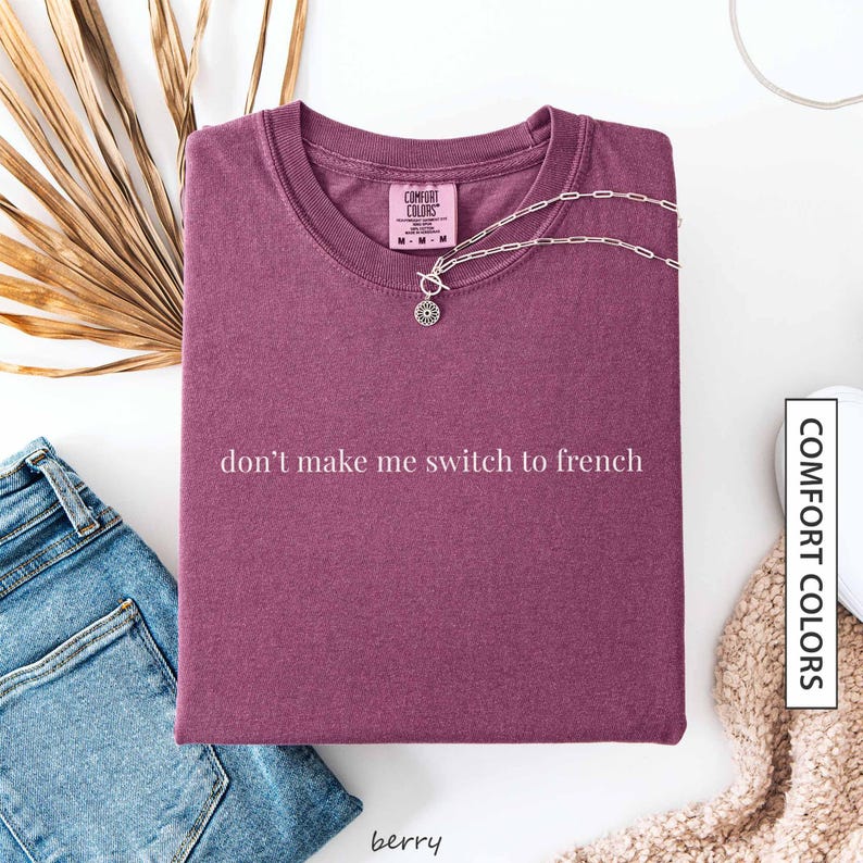 a purple t-shirt with the text "don't make me switch to french" printed on it, along with a necklace and some other clothing items.