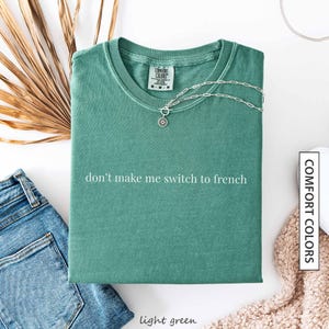 a green t-shirt with the text "don't make me switch to french" printed on it, along with a necklace and some other clothing items.
