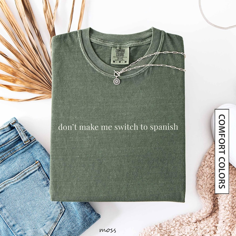 a green t-shirt with the text "don't make me switch to spanish" printed on it, along with a necklace and some other clothing items.