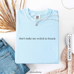 a light blue t-shirt with the text "don't make me switch to french" printed on it, along with a necklace and some other clothing items.