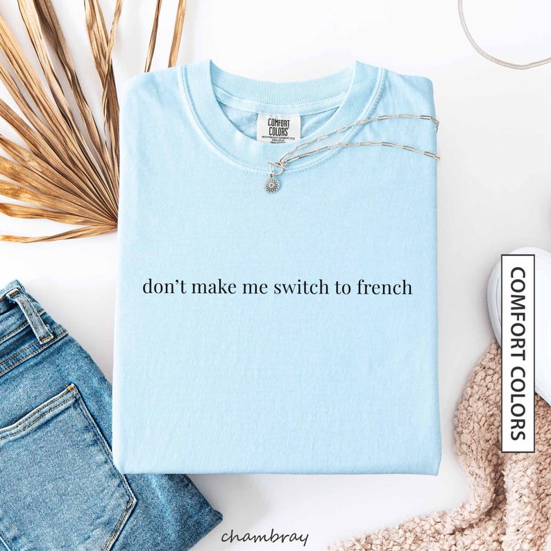a light blue t-shirt with the text "don't make me switch to french" printed on it, along with a necklace and some other clothing items.