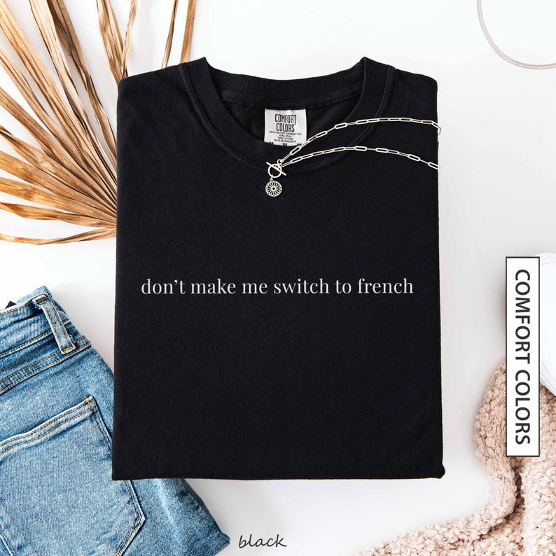 a black t-shirt with the text "don't make me switch to french" printed on it, along with a necklace and some jeans.