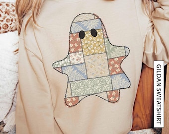 May include: A sand-coloured Gildan sweatshirt with a patchwork ghost design. The ghost is made of floral and patterned fabric squares in pastel colours, with black oval eyes. The sweatshirt has the text "GILDAN SWEATSHIRT" on the side.