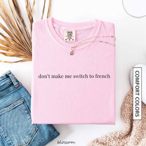 a pink t-shirt with the text "don't make me switch to french" printed on it, along with a necklace and some other clothing items.