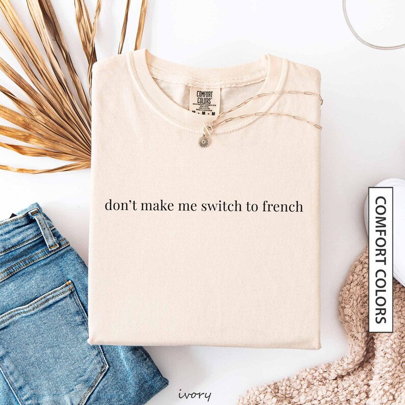 a white t-shirt with the text "don't make me switch to french" printed on it, along with a necklace and some other clothing items.