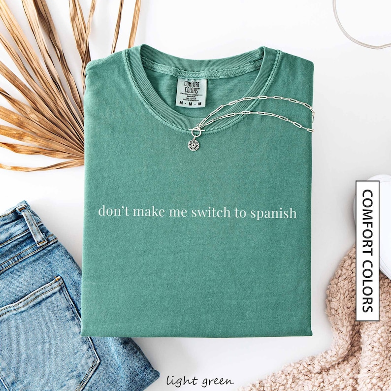 a green t-shirt with the text "don't make me switch to spanish" printed on it, along with a necklace and some other clothing items.