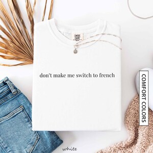 a white t-shirt with the text "don't make me switch to french" printed on it, along with a pair of blue jeans and a beige sweater.