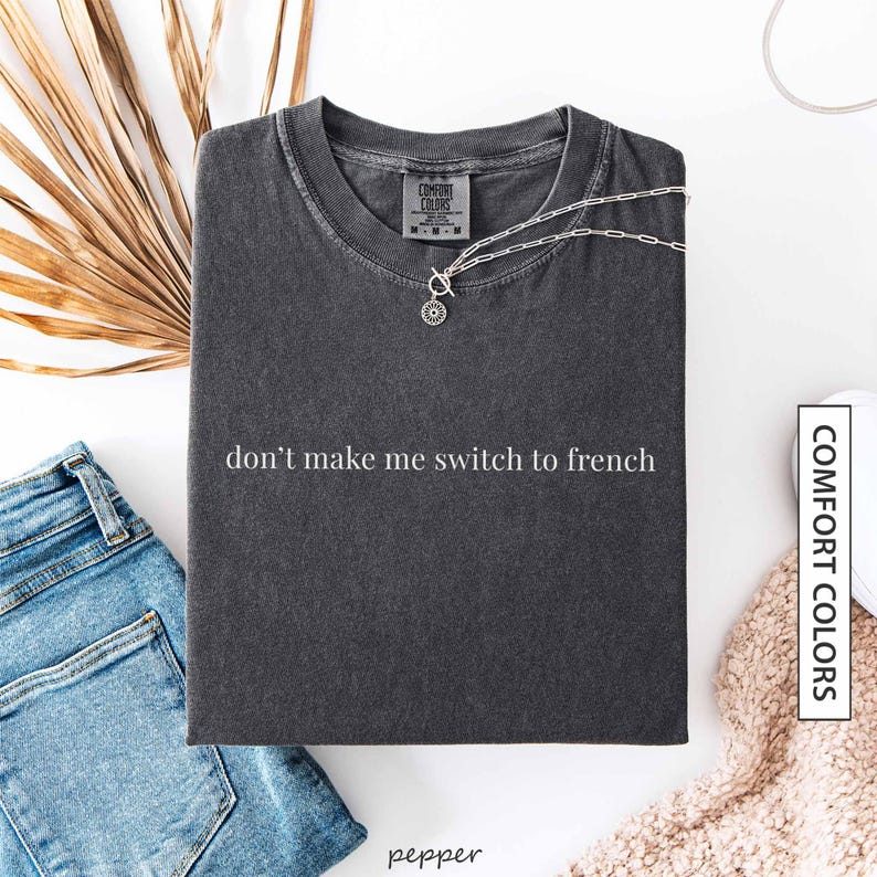 a gray t-shirt with the text "don't make me switch to french" printed on it, along with a denim jacket and a pair of jeans.