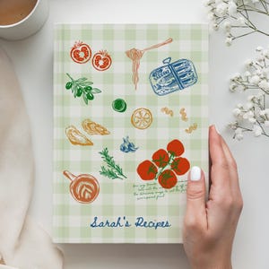 Peut inclure: Un carnet de recettes à couverture rigide avec un motif vichy vert clair et blanc. La couverture présente des illustrations colorées de tomates, d'une boîte de sardines, d'olives, d'herbes et de pâtes. Le texte "Sarah's Recipes" est en bleu.
