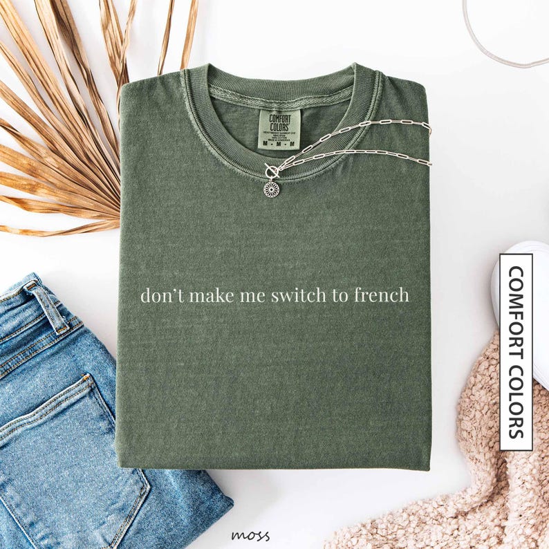 a green t-shirt with the text "don't make me switch to french" printed on it, along with a necklace and some other clothing items.