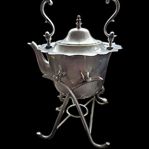 May include: A silver teapot with a wooden handle and a decorative stand. The teapot has a fluted design and a round lid with a finial.