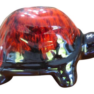 May include: A ceramic turtle ornament with a glossy finish. The shell is a blend of red and black, with a textured appearance. The head, feet, and underside are black. A decorative item.