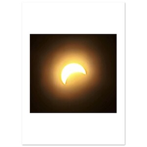 May include: A photograph of a partial solar eclipse. The sun is a bright yellow crescent shape against a dark background, with a soft glow surrounding it. The image is framed by a white border.