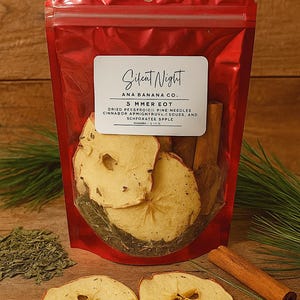 May include: A red cellophane bag containing dried apple slices, cinnamon sticks, and pine needles. The bag has a label that reads "Silent Night" and "5 Mmer Eot". The ingredients are for a simmer pot.