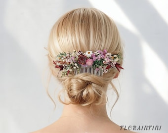 Puede incluir: Un peine para el cabello floral con una variedad de flores secas en tonos burdeos, rosa y blanco. El peine es de metal plateado y está adornado con pequeñas flores y vegetación. El texto "FLORAINFINI" es visible en la esquina inferior derecha.