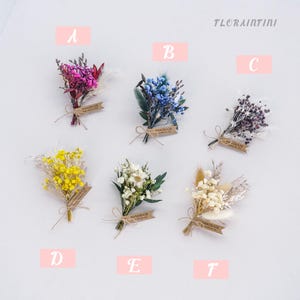 Puede incluir: Una colección de seis pequeños ramos de flores secas hechos a mano. Cada ramo presenta una mezcla única de colores, incluyendo rosa, azul, amarillo, blanco y crema. Cada ramo está atado con hilo y tiene una etiqueta "handmade".