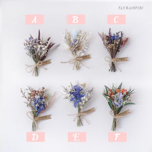 Op de afbeelding: Zes kleine boeketten van gedroogde bloemen, elk vastgebonden met touw en een "handmade" label. De boeketten bevatten een verscheidenheid aan kleuren, waaronder blauw, paars, wit en oranje. De afbeelding heeft de tekst "FLORAINTINI" in de rechterbovenhoek.