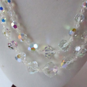 May include: A multi-strand necklace made of clear iridescent glass beads. The beads are faceted and have a rainbow sheen.