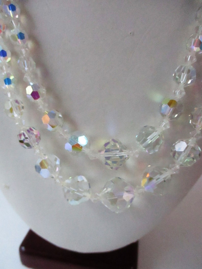 May include: A multi-strand necklace made of clear iridescent glass beads. The beads are faceted and have a rainbow sheen.