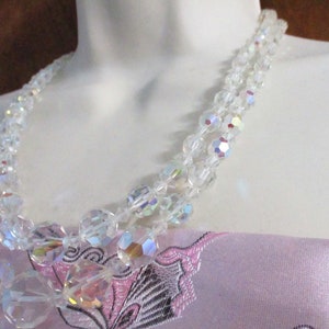 May include: A double strand iridescent crystal necklace with clear faceted beads. The necklace is on a white mannequin bust.