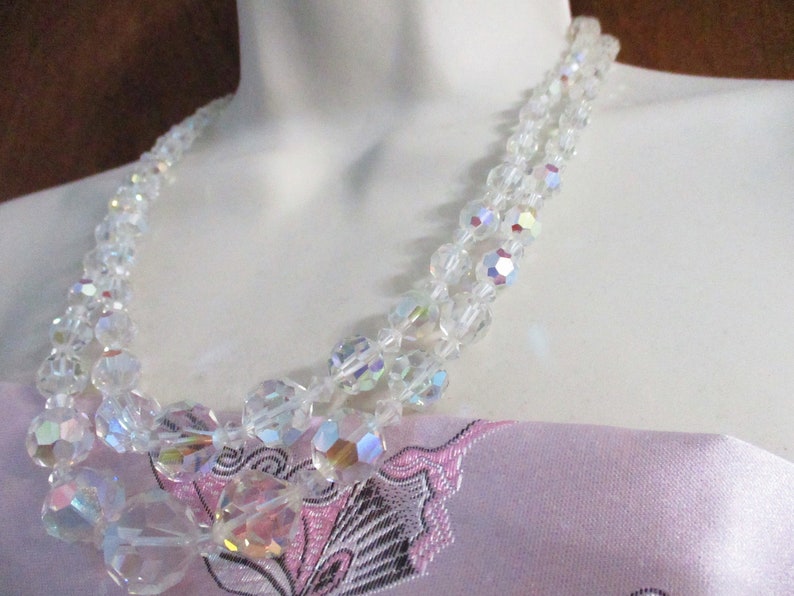 May include: A double strand iridescent crystal necklace with clear faceted beads. The necklace is on a white mannequin bust.