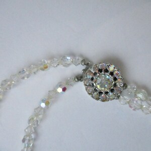 May include: A white crystal beaded necklace with a silver clasp featuring a large iridescent crystal in the centre.