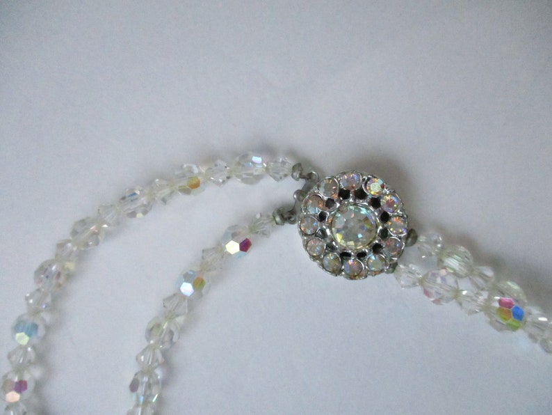 May include: A white crystal beaded necklace with a silver clasp featuring a large iridescent crystal in the centre.