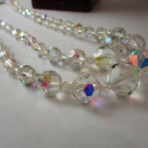 May include: A double strand necklace made of clear iridescent glass beads. The beads are faceted and have a rainbow sheen.