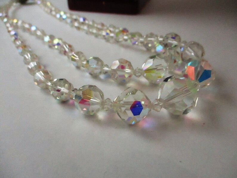 May include: A double strand necklace made of clear iridescent glass beads. The beads are faceted and have a rainbow sheen.
