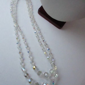 May include: A double strand necklace made of clear iridescent glass beads. The beads are faceted and have a slightly rounded shape. The necklace is approximately 18 inches long.