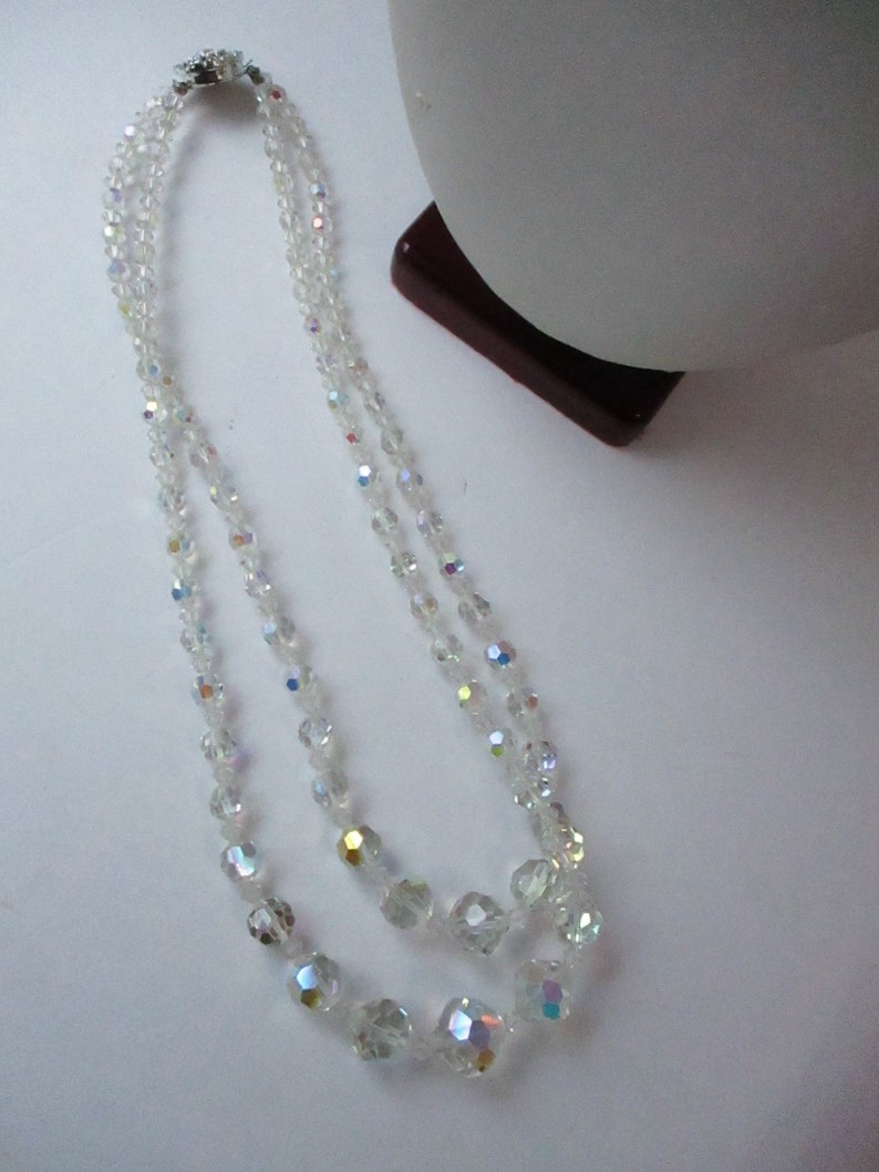 May include: A double strand necklace made of clear iridescent glass beads. The beads are faceted and have a slightly rounded shape. The necklace is approximately 18 inches long.