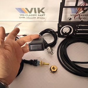 May include: A selection of car parts, featuring a black control module with a silver button, a temperature sensor, and a black cable. The image also shows a car dashboard component and the text "VIK CLASSIC PART".