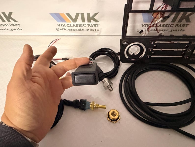 May include: A selection of car parts, featuring a black control module with a silver button, a temperature sensor, and a black cable. The image also shows a car dashboard component and the text "VIK CLASSIC PART".