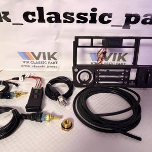 May include: A selection of car parts, including a black dashboard frame, wiring harnesses, sensors, and a brass fitting. The components are displayed on a white surface, with the "VIK CLASSIC PART" logo visible.