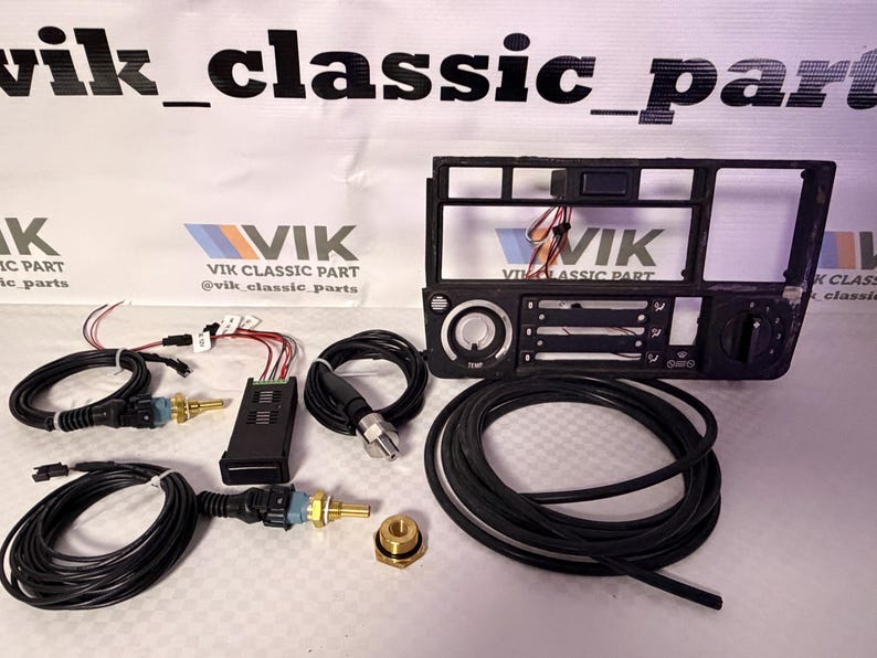 May include: A selection of car parts, including a black dashboard frame, wiring harnesses, sensors, and a brass fitting. The components are displayed on a white surface, with the "VIK CLASSIC PART" logo visible.
