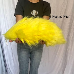 Op de afbeelding: Een felgeel imitatiebont staartaccessoire met een zilverkleurige metalen sluiting aan één uiteinde. De lange, pluche synthetische vezels creëren een volumineuze textuur en de tekst Faux Fur is zichtbaar in de rechterbovenhoek van de afbeelding.