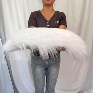 May include: A long, fluffy, white faux fur tail accessory featuring a silver-toned metal clip attachment at the base. The tail has a thick, layered texture with long, soft synthetic fibers that taper toward the end, creating a voluminous appearance.