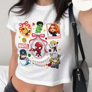 May include: White crop top with a colorful graphic print of various Marvel characters, including Spider-Man, Iron Man, Hulk, Black Widow, Captain America, and Thor. The graphic includes the word "MARVEL" and a red ribbon with a bow.