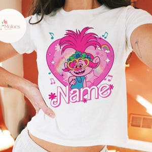 May include: White t-shirt with a pink heart design featuring a cartoon character with pink hair, blue eyes, and a blue shirt. The text "Name" is written in pink letters below the character.