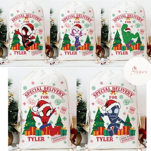 May include: White canvas Christmas gift bags with drawstring closures. Each bag features a superhero graphic, the text "SPECIAL DELIVERY FOR" and the name "TYLER". The bags are decorated with Christmas trees, gifts, snowflakes, and a "SANTA CLAUS APPROVED" stamp.